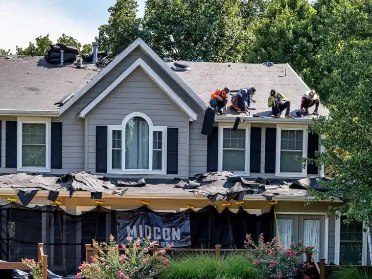 Midcon crew replacing the roof of a gray two-story home, Midcon banner hung over the porch